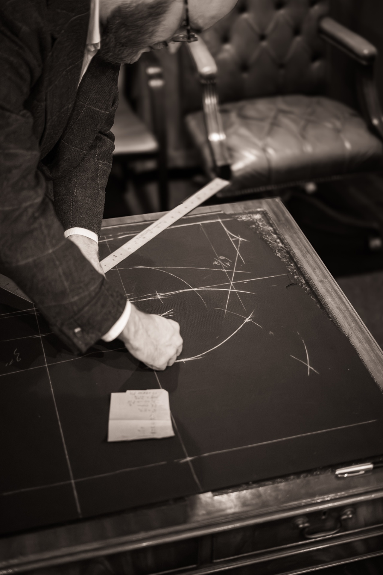 A tailor drawing a pattern in chalk on dark cloth with a wooden rule